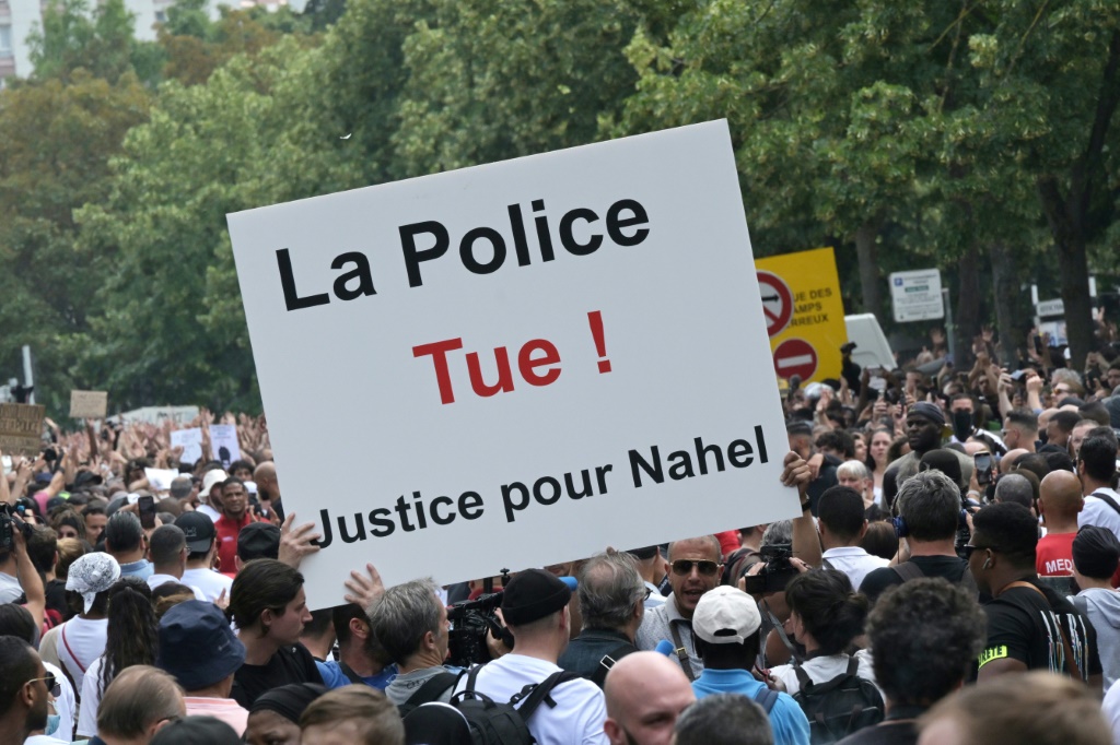 متظاهر يحمل لافتة مكتوب عليها بالفرنسية "الشرطة تقتل! العدالة لنائل" في نانتير في ضواحي باريس في 29 حزيران/يونيو 2023 بعد قتل شرطي لمراهق يبلغ 17 عامًا أثناء عملية تفتيش مروري (ا ف ب)