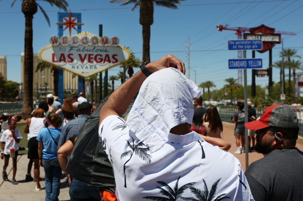 رجل يحمي نفسه من أشعة الشمس أثناء انتظاره في طابور لالتقاط صورة أمام لافتة "مرحباً بكم في لاس فيغاس" خلال موجة الحر في 14 تموز/يوليو 2023 (ا ف ب)