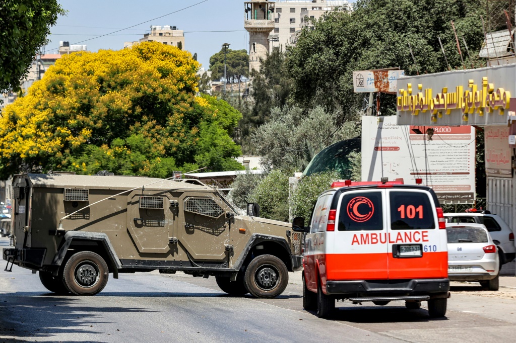 مركبة إسعاف تابعة لجمعية الهلال الأحمر الفلسطيني تحاول المرورو قرب مركبة عسكرية إسرائيلية تغلق الطريق بالتزامن مع غارة عسكرية للجيش الإسرائيلي في مخيم العين للاجئين الفلسطينيين غرب نابلس في الضفة الغربية المحتلة في 26 تموز/يوليو 2023 (ا ف ب)  &nbsp;