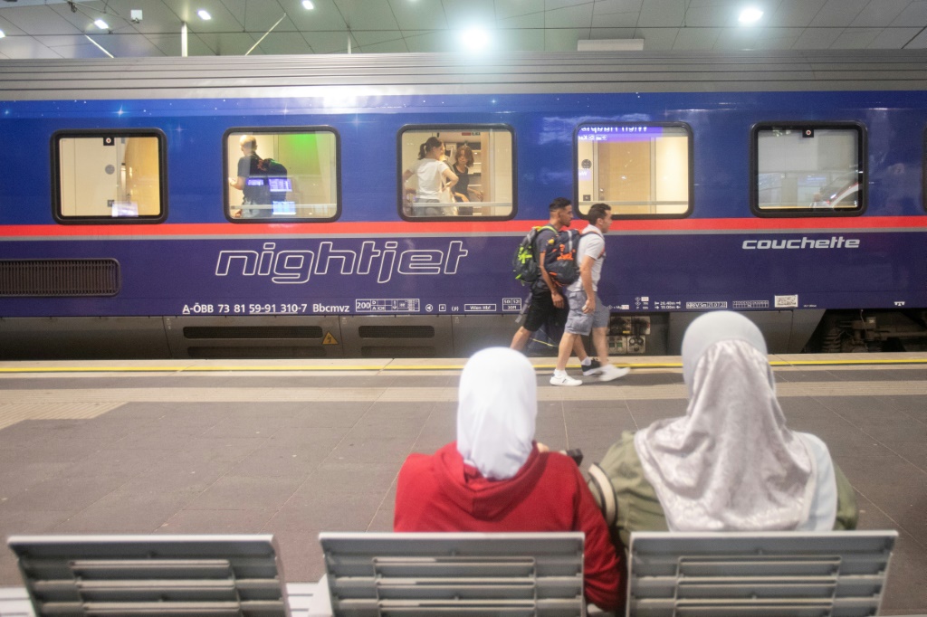    امرأتان على مقعد على في محطة القطارات أمام عربة قطار ليلي في فيينا في 25 تموز/يوليو 2023. (أ ف ب)   