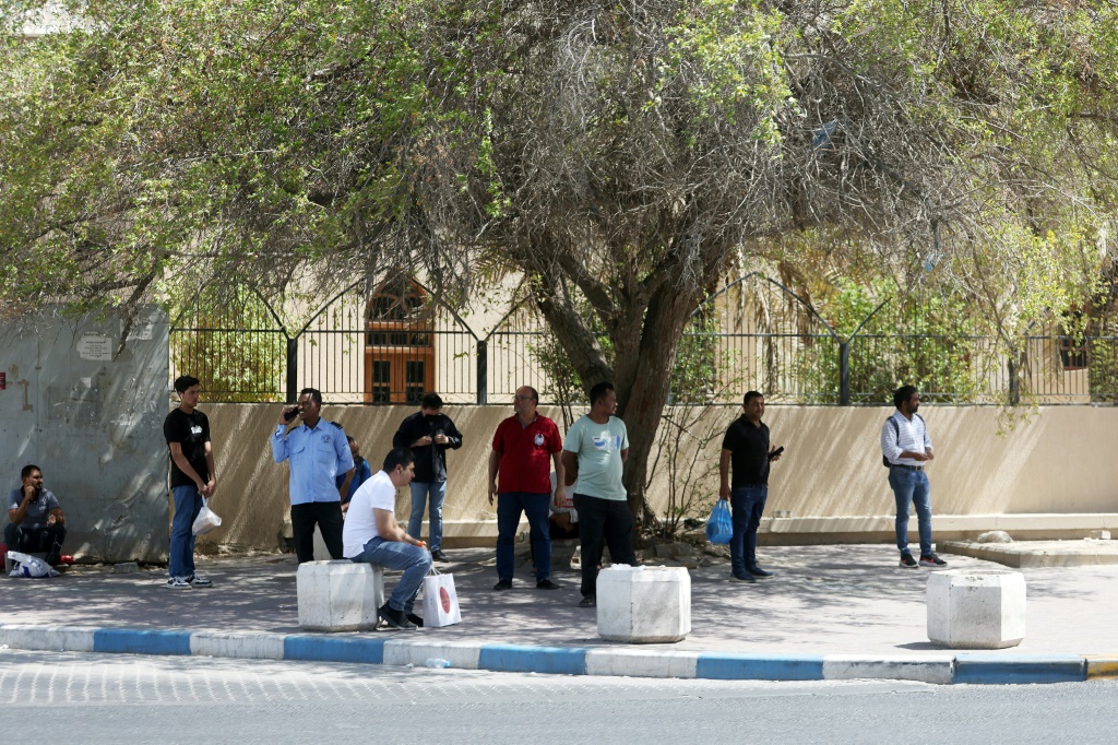 أشخاص يحاولون حماية أنفسهم من الشمس في ظل شجرة في العاصمة الكويتية بتاريخ 30 تموز/يوليو 2023 (ا ف ب)