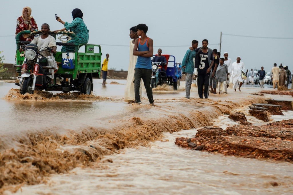 أشخاص يسيرون ويقودون سياراتهم عبر مياه الفيضانات الموحلة على طول الشارع بعد هطول أمطار غزيرة في منطقة سقاعي بالقرب من أم درمان في 5 آب/أغسطس 2023 (ا ف ب)