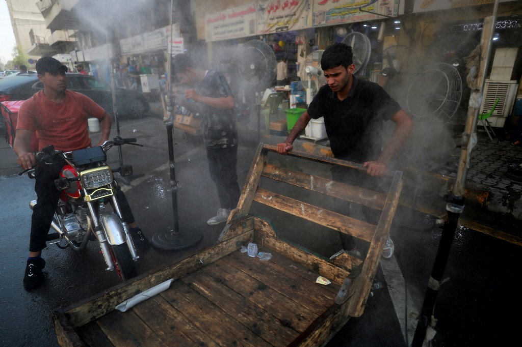 رجال يحاولون تبريد أجسامهم برذاذ المياه وسط القيظ في شارع ببغداد (ا ف ب)