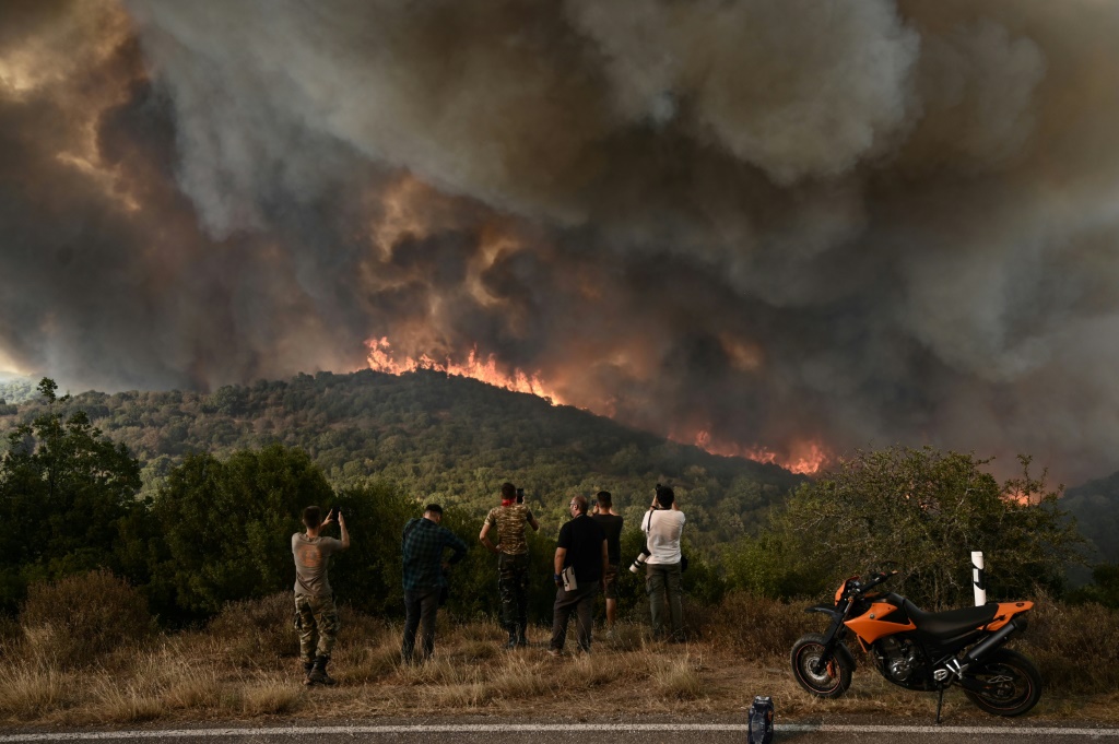 الناس ينظرون إلى حرائق الغابات المشتعلة في غابة في شمال اليونان (أ ف ب)