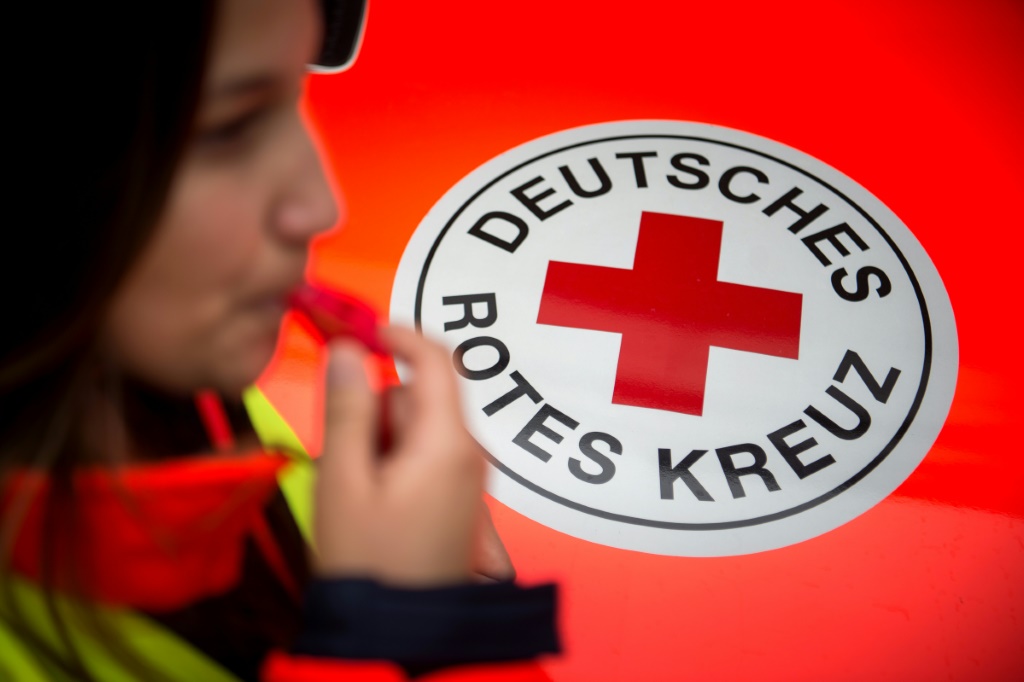 إحدى أعضاء الصليب الاحمر تقف أمام شعار للمنظمة في شتوتغارت بتاريخ 14 أيار/مايو 2018 (ا ف ب)