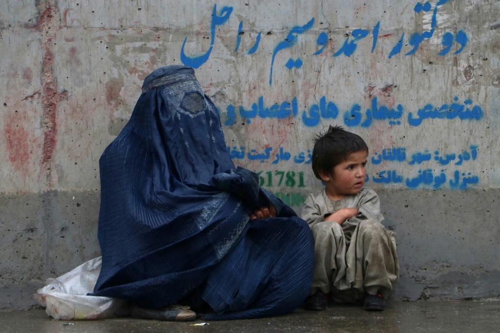امراة وطفل يجلسان على طريق بعد هطول المطر في منطقة فايز اباد بولاية بدخشان في 27 آب/اغسطس 2023. (ا ف ب)   