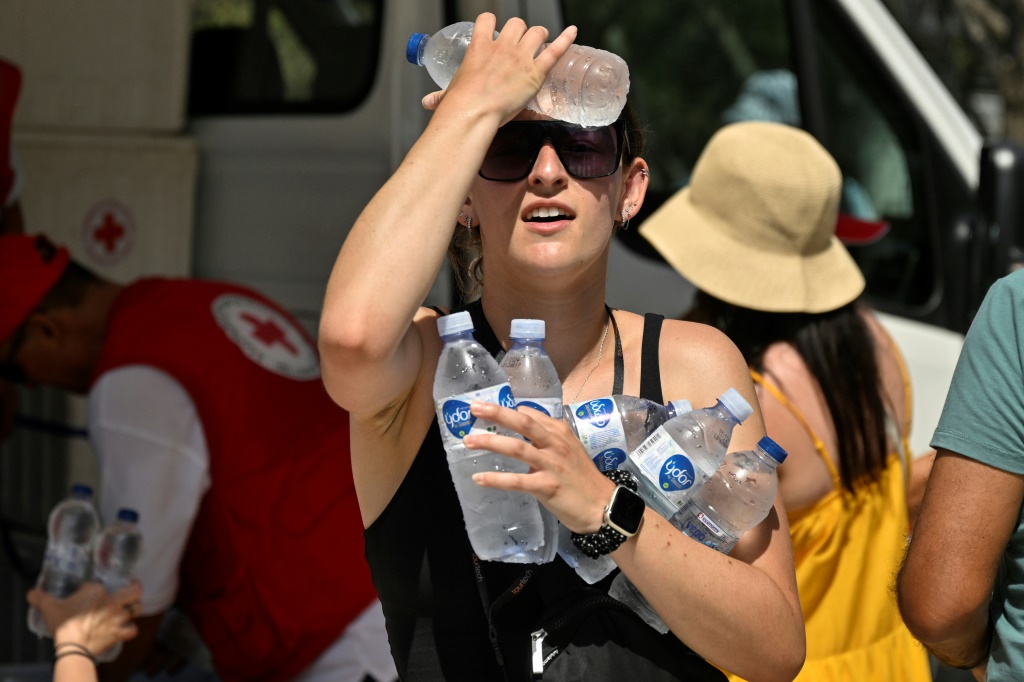 امرأة تبرّد وجهها بزجاجات مياه باردة وزّعها الصليب الأحمر اليوناني قرب مدخل موقع أكروبوليس الأثري في أثينا في 20 تموز/يوليو 2023 وسط موجة حر شديد (ا ف ب)