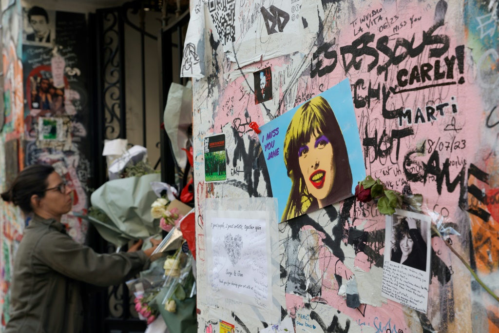 امرأة تضع الزهر أمام مدخل منزل المغني الفرنسي الراحل سيرج غينسبور في باريس في 20 تموز/يوليو 2023 عقب وفاة زوجته السابقة جين بيركين (ا ف ب)