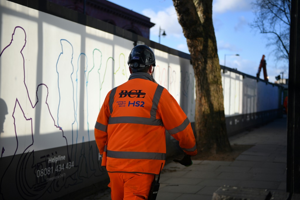 عامل بناء يسير خارج موقع بناء لقسم من مشروع السكك الحديدية عالية السرعة في بريطانيا HS2 في محطة قطار لندن يوستون (أ ف ب)   