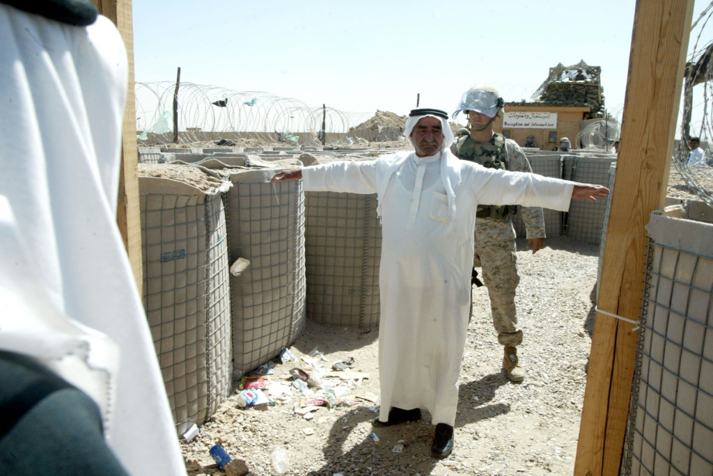 جندي من مشاة البحرية الأمريكية يقوم بتفتيش رجل عراقي يدخل سجن أبو غريب لزيارة أحد أقاربه في مايو 2004 (أ ف ب)   