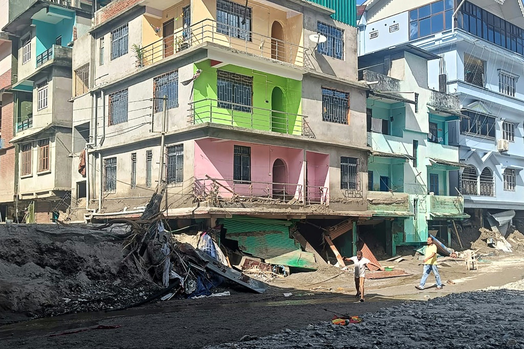سكان يسيرون على طول شارع مغطى بالطين والحطام بالقرب من المباني المتضرّرة في رانغبو في 6 تشرين الأول/أكتوبر 2023، بعد فيضان مفاجئ ناجم عن ارتفاع مستوى بحيرة جليدية (ا ف ب)