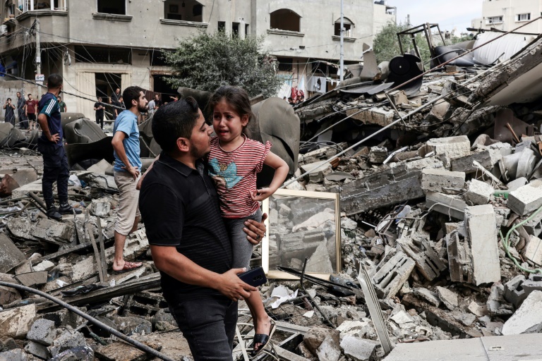 رجل يحمل طفلا قرب مبنى مدمر نتيجة القصف الإسرائيلي في مدينة غزة في 7 تشرين الأول/أكتوبر 2023 (أ ف ب)