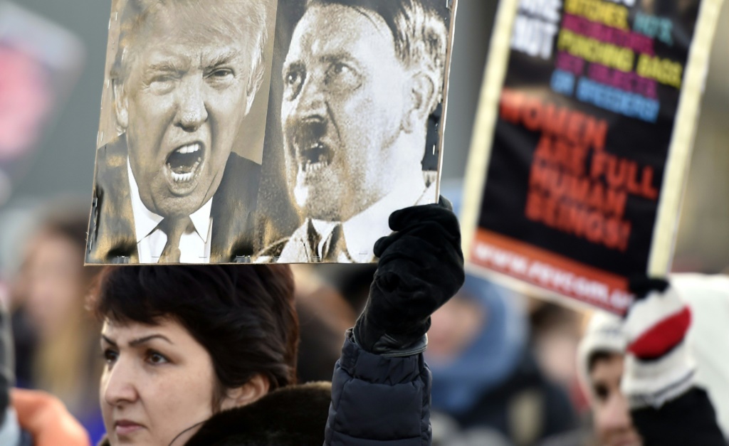     إحدى المشاركات في مسيرة نسائية في هلسنكي تحمل ملصقًا يصور الرئيس الأمريكي دونالد ترامب والديكتاتور الألماني أدولف هتلر في 21 يناير 2017، بعد يوم واحد من تنصيب الرئيس الأمريكي (أ ف ب)   