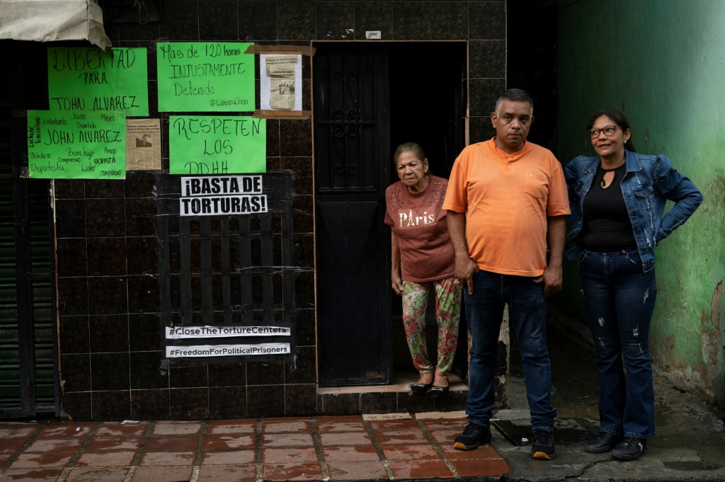 أفراد من عائلة ألفاريز يقفون أمام ملصقات تطالب بالإفراج عن جون ألفاريز، في حي سان مارتن في كاراكاس، في أكتوبر 2023 (ا ف ب)   