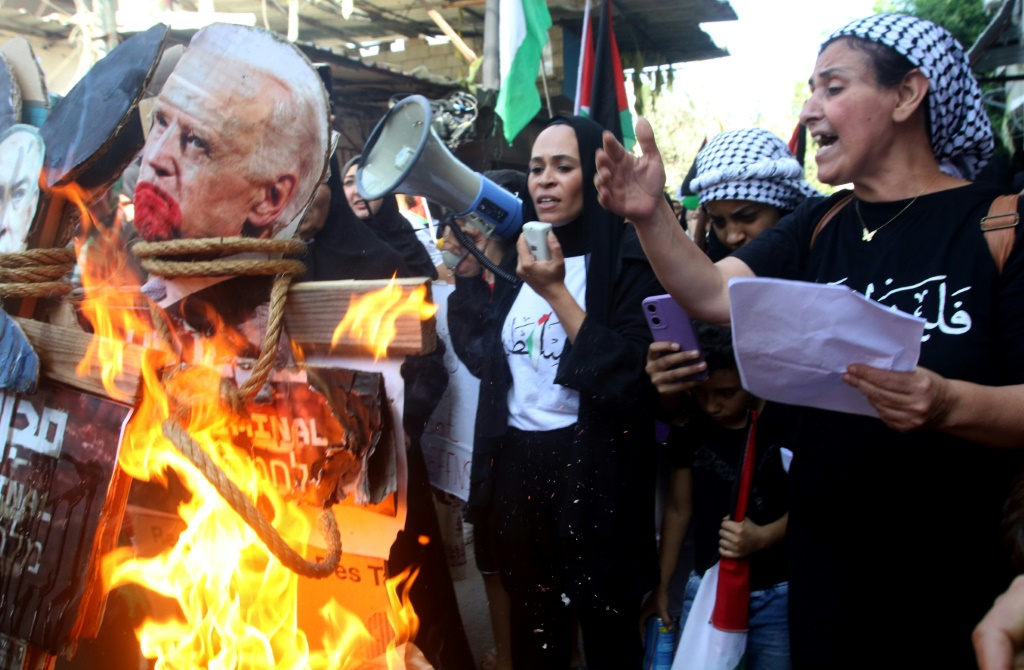 امرأة تتحدث وبجانبها صورة للرئيس الأميركي جو بايدن تحترق أثناء احتجاج في مخيم عين الحلوة للاجئين الفلسطينيين بالقرب من مدينة صيدا الساحلية بجنوب لبنان في 18 تشرين الأول/أكتوبر 2023 (ا ف ب)