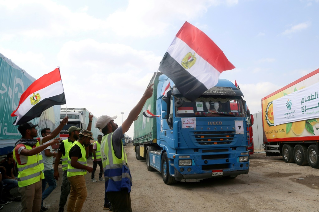 أشخاص على الجانب المصري من معبر رفح الحدودي يلوحون بالأعلام أثناء عبور قافلة من الشاحنات المحملة بالمساعدات الإنسانية إلى قطاع غزة (أ ف ب)  &nbsp;