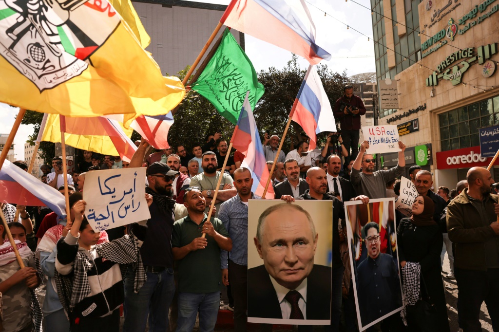 أشخاص يلوحون بأعلام روسيا وفلسطين وفتح وحماس ويحملون صور الرئيس الروسي فلاديمير بوتين وزعيم كوريا الشمالية كيم جونغ أون في شوارع مدينة الخليل بالضفة الغربية المحتلة (أ ف ب)   