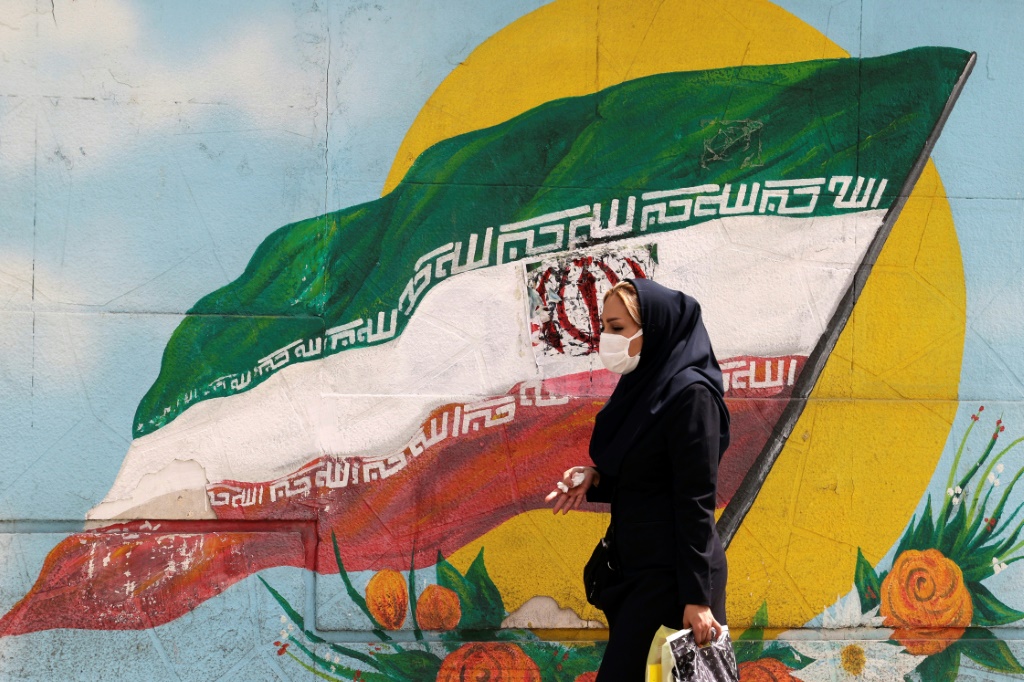 امرأة إيرانية تمشي قرب جدار مرسوم عليه علم إيراني في طهران في 10 نيسان أبريل 2023 (ا ف ب)