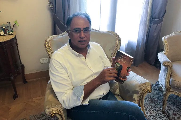 الروائي والقاضي المصري أشرف العشماوي يحمل في يده أحدث رواياته "السرعة القصوى صفر" (الجزيرة)
