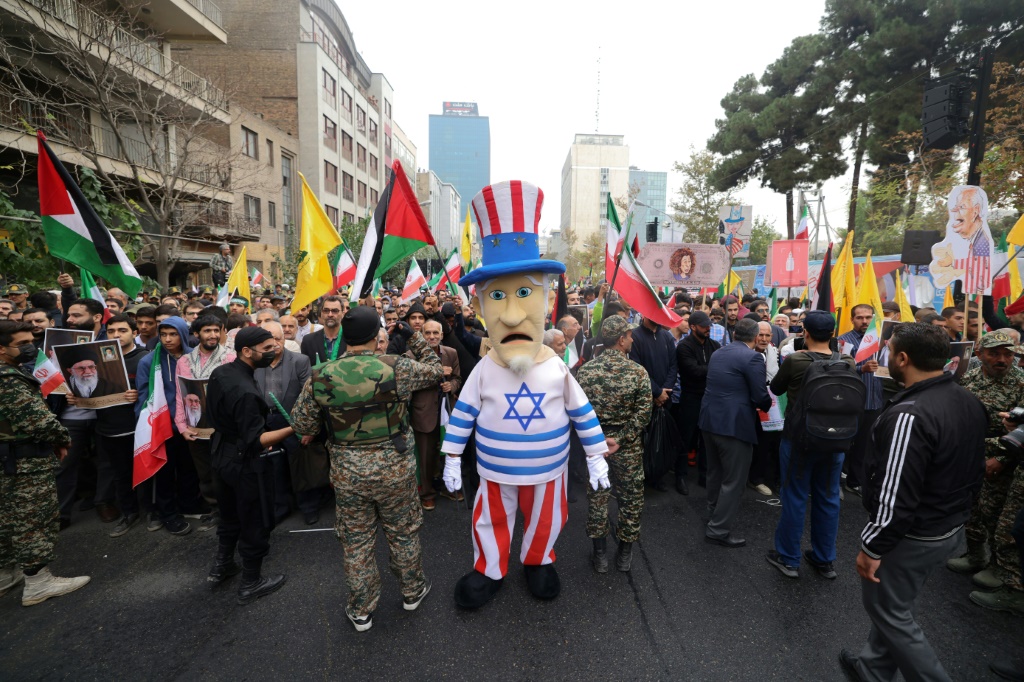 رجل يرتدي زيّ "العم سام" الأميركي مع قميص عليه العلم الإسرائيلي في تجمّع أمام المقر السابق للسفارة الأميركية في طهران دعمًا للفلسطينيين في قطاع غزة في الرابع من تشرين الثاني/نوفمبر 2023 (أ ف ب)   
