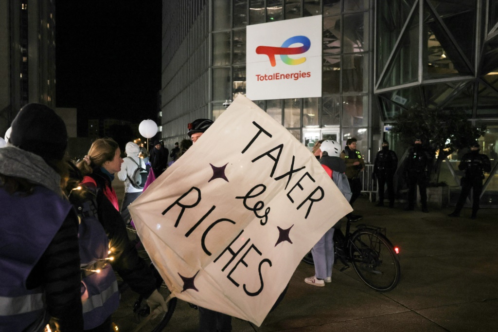 متظاهر يحمل لافتة مكتوب عليها بالفرنسية "افرضوا ضرائب على الأثرياء" في مسيرة أمام مقر "توتال إنرجي" في حيّ لا ديفانس في كوربوفوا في فرنسا في الثالث من تشرين الثاني/نوفمبر 2023 (أ ف ب)   