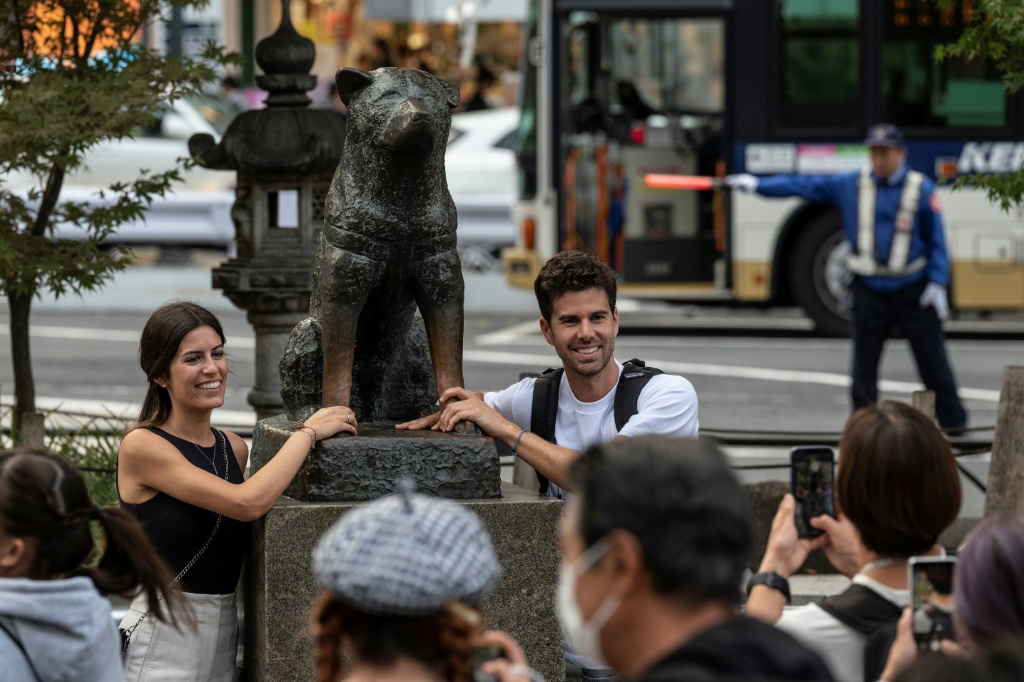 زوجان يقفان لالتقاط الصور بجوار تمثال "هاتشيكو" أمام محطة شيبويا بطوكيو (ا ف ب)