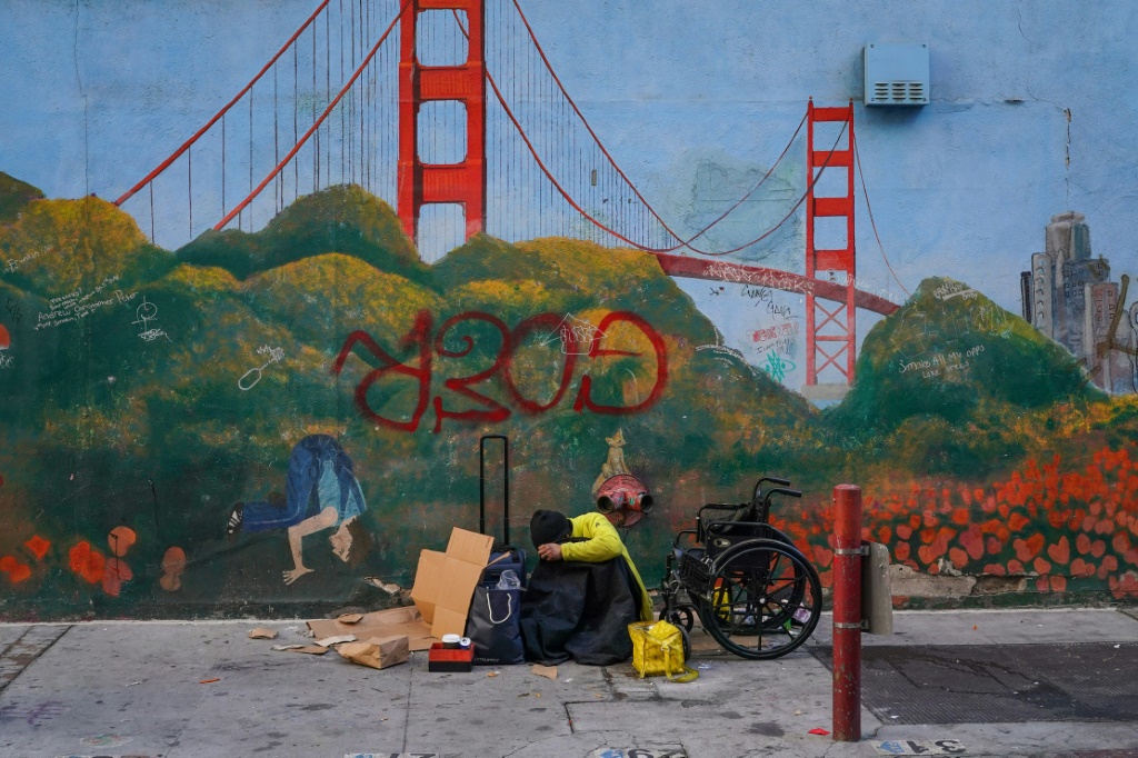 شخص بلا مأوى يتكئ على لوحة جدارية لجسر جولدن جيت بالقرب من مقر قمة أبيك في سان فرانسيسكو، كاليفورنيا في 11 نوفمبر 2023 (أ ف ب)   