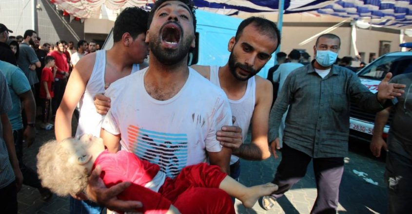 رجل يصرخ وهو يحمل طفلاً صغيراً يهرع إلى مستشفى الشفاء إثر القصف الذي شنته طائرات اسرائيل في غزة  (أ ف ب)