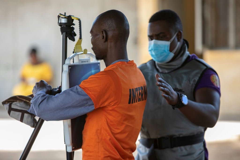 أحد أفراد الطاقم الطبي يساعد سجيناً يقف أمام جهاز محمول للفحص بالأشعة السينية متّصل ببرنامج للذكاء الاصطناعي، في باحة سجن مابوتو في موزمبيق بتاريخ السادس من تشرين الثاني/نوفمبر 2023 (ا ف ب)