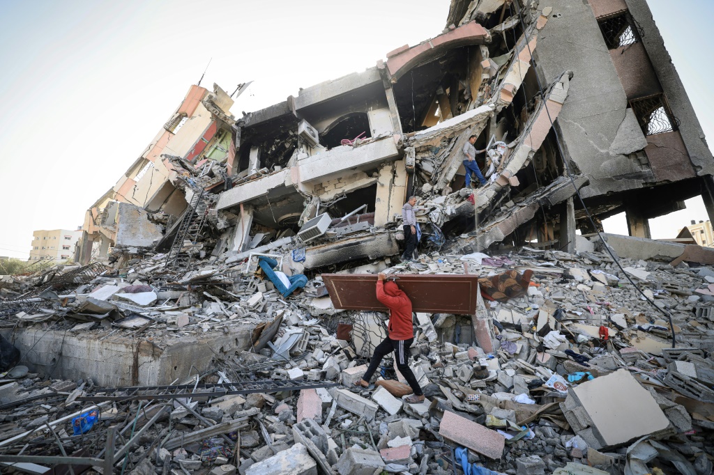 فلسطينيون يحملون بعض مقتنياتهم يسيرون وسط أنقاض المباني المدمرة في حيّ الزهراء بالضواحي الجنوبية لمدينة غزة في 26 تشرين الثاني/نوفمبر 2023 مع دخول الهدنة بين إسرائيل وحماس يومها الثالث (أ ف ب)   