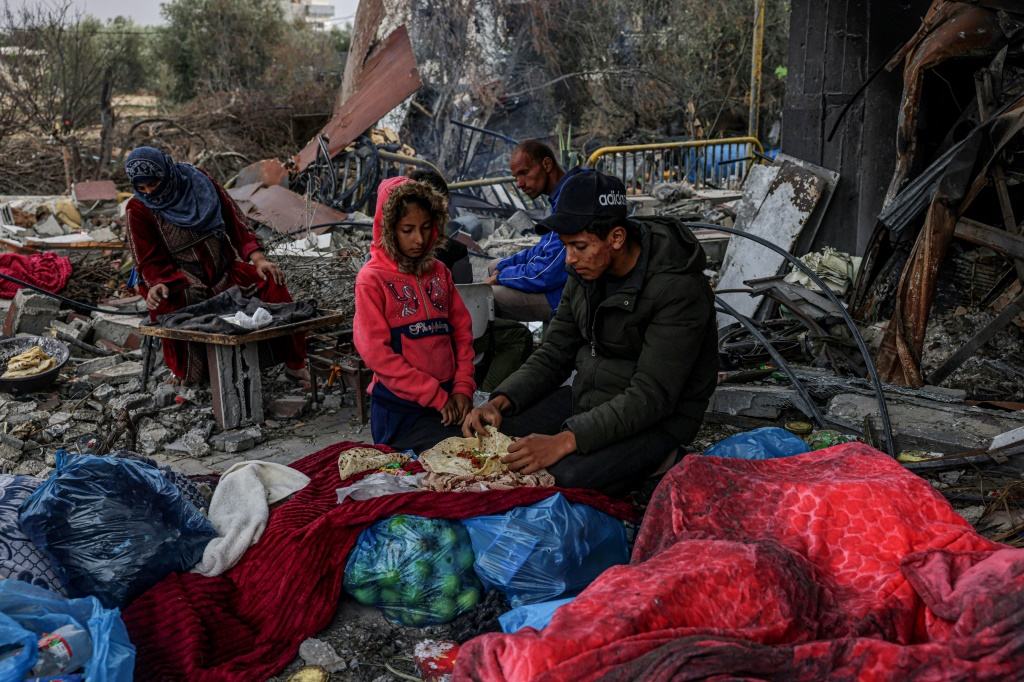 فلسطينيون يتناولون الطعام في الخارج وسط الدمار الذي خلفته الغارات الإسرائيلية على قطاع غزة (ا ف ب)   