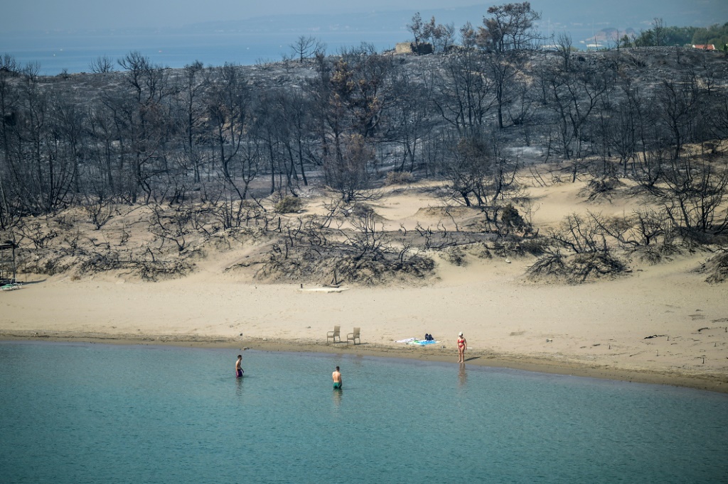 – صور العام 2023 لوكالة فرانس برس – امرأة تدخل البحر من شاطئ دمرت فيه حرائق الغابات الغابات، في جليسترا بالقرب من قرية جينادي في الجزء الجنوبي من جزيرة رودس اليونانية، في 27 يوليو 2023. (أ ف ب)