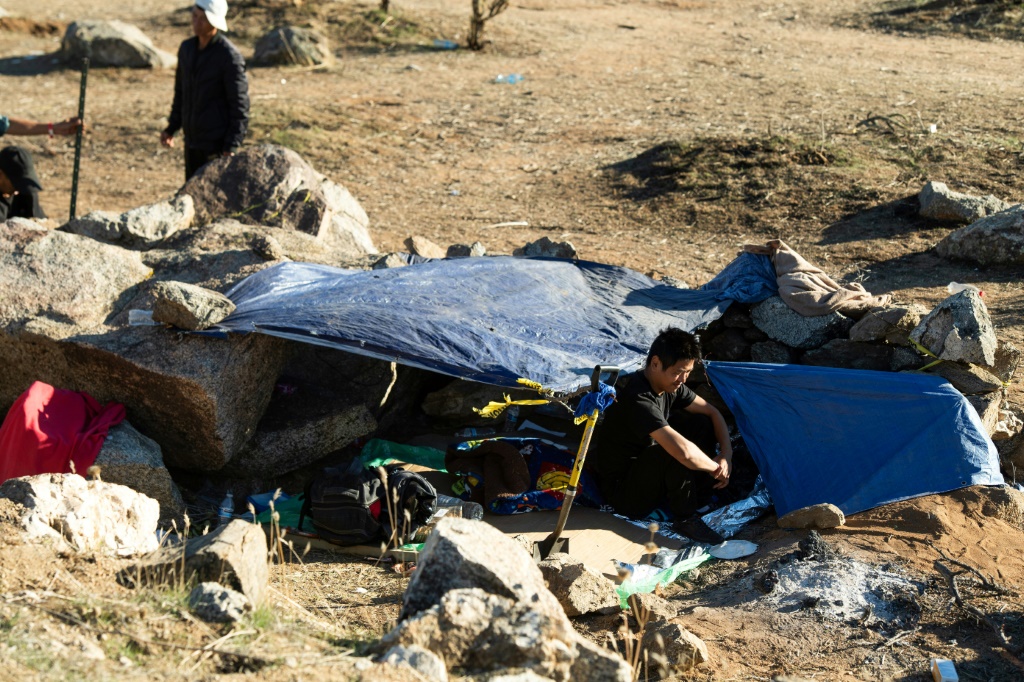 مهاجر صيني يجلس أمام خيمته في مخيم للمهاجرين على الجانب الأمريكي من الجدار الحدودي الذي يفصل المكسيك عن الولايات المتحدة في جاكومبا، كاليفورنيا، 6 ديسمبر 2023 (أ ف ب)   