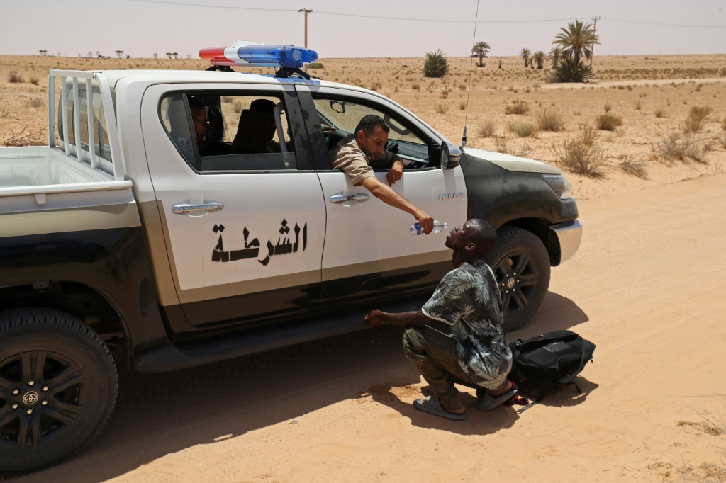 أحد حرس الحدود الليبي يقدم الماء لمهاجر خلال عملية إنقاذ بالقرب من الحدود مع تونس (أ ف ب)   