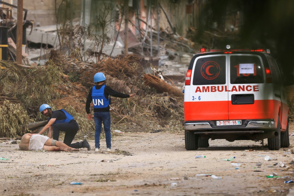    عاملان لدى الأمم المتحدة يقتربان من فلسطيني مصاب بنيران إسرائيلية لنقله إلى سيارة إسعاف في حيّ الزيتون في قطاع غزة في 25 تشرين الثاني/نوفمبر 2023 (أ ف ب)   