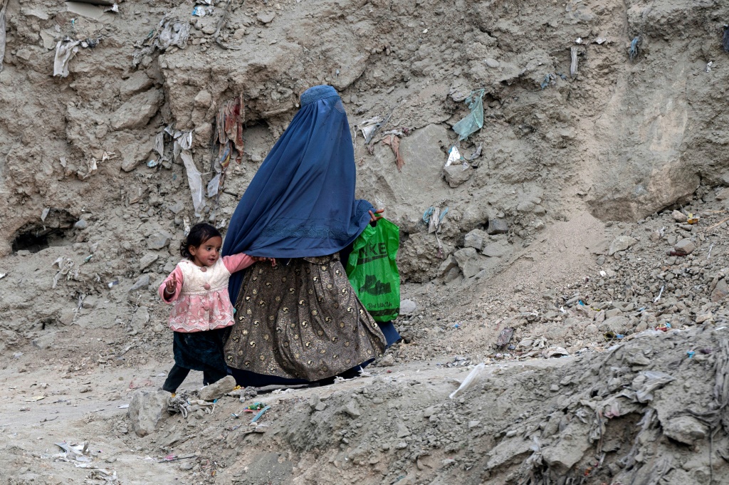 امرأة أفغانية ترتدي البرقع تسير مع فتاة على طول طريق في منطقة في كابول في 21 تشرين الثاني/نوفمبر 2023 (أ ف ب)   