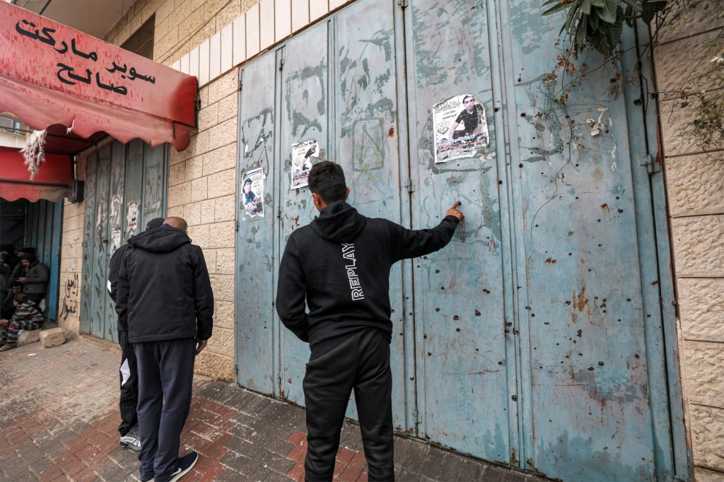 فلسطينيون يتفقدون الثقوب التي أحدثها الرصاص في أبواب متجر في بلدة عزون بالضفة الغربية بعد أن نفذت القوات الإسرائيلية غارة دامية (أ ف ب)   