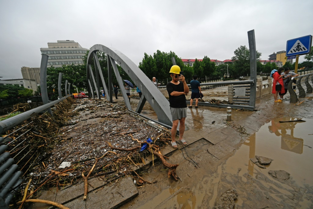 أشخاص يسيرون في شارع غمرته المياه في بكين جراء أمطار غزيرة غير مسبوقة في 31 تموز/يوليو 2023 (أ ف ب)   