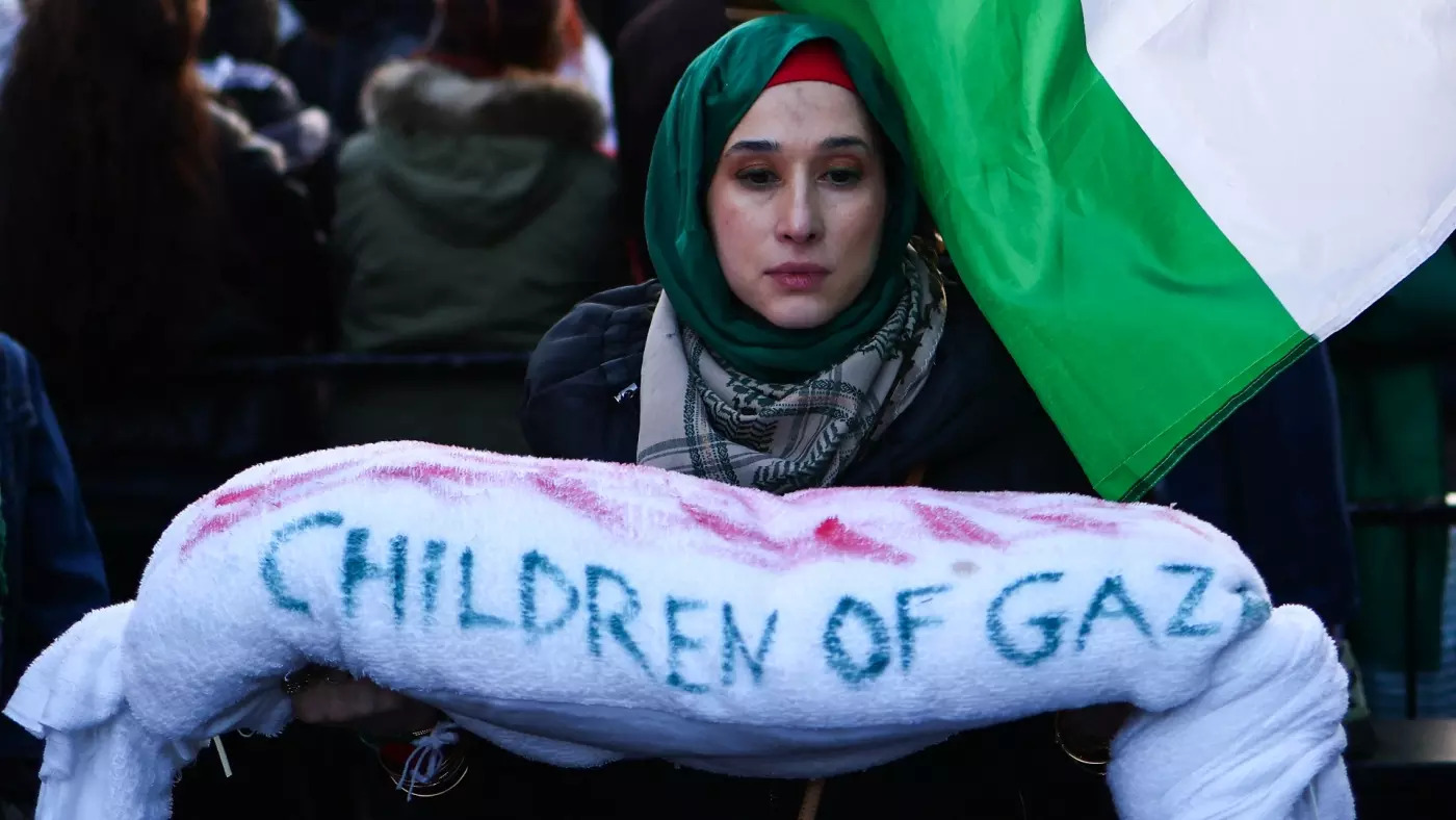 متظاهرة يحمل طفلاً فلسطينيًا متوفى ومكفنًا بشكل رمزي أثناء مشاركته في مسيرة تطالب بوقف إطلاق النار في غزة، في وسط لندن في 9 ديسمبر 2023 (أ ف ب)