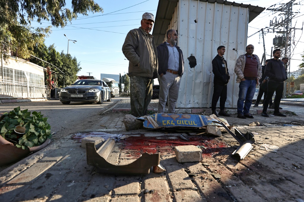 أشخاص ينظرون إلى بركة من الدماء حيث قُتل ستة فلسطينيين خلال غارة إسرائيلية في جنين بالضفة الغربية المحتلة . (ا ف ب)