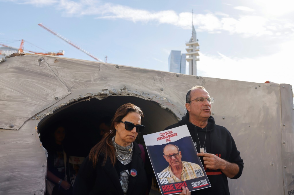 إسرائيليان يحملان صورة قريب لهما احتجزته حماس، يقفان أمام نموذج من أنفاق حماس، تم تركيبه في تل أبيب.(ا ف ب)