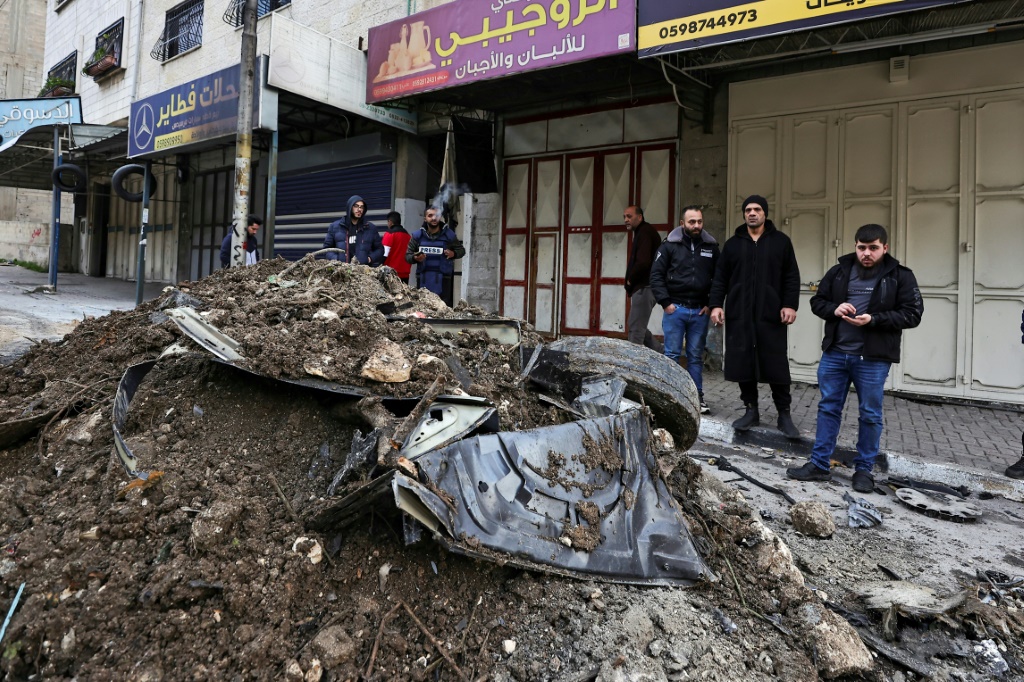 فلسطينيون يتفحصون حطام سيارة استهدفتها غارة جوية إسرائيلية استهدفت ناشطا بارزا بالقرب من مخيم بلاطة للاجئين في مدينة نابلس بالضفة الغربية (ا ف ب)