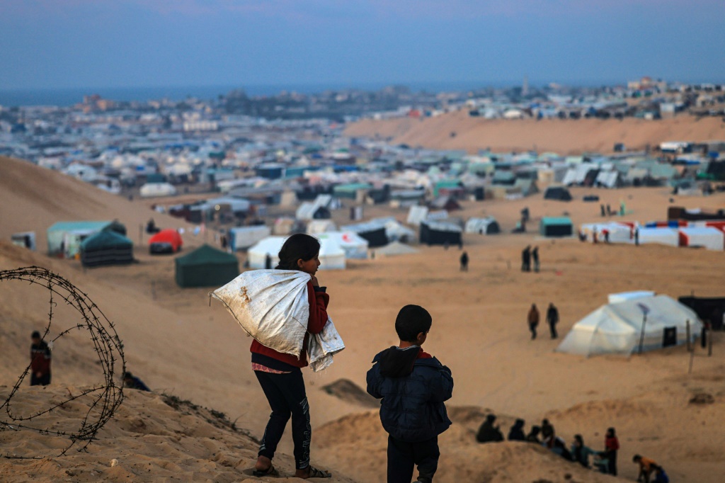 طفلان فلسطينيان نازحان يسيران على تلة مقابل مخيمهم في رفح جنوب قطاع غزة في 19 كانون الثاني/يناير 2024 (ا ف ب)