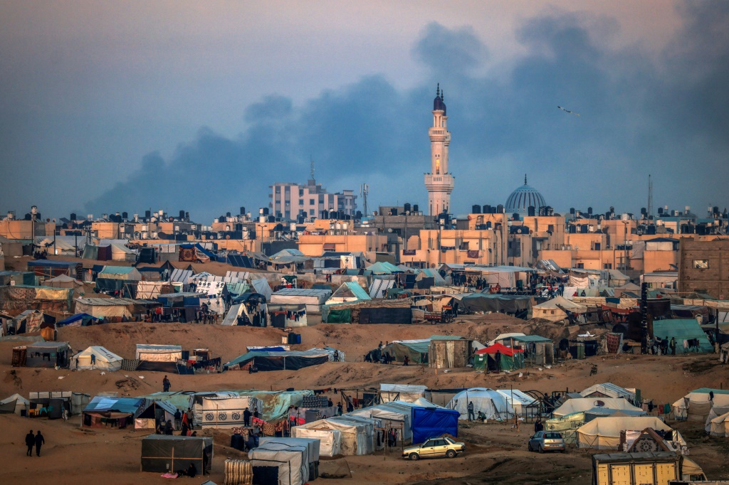 صورة لمخيم مؤقت للنازحين الفلسطينيين غرب رفح بالقرب من الحدود المصرية تظهر الدخان يتصاعد في خان يونس بعد القصف الإسرائيلي في 19 كانون الثاني/يناير 2024، وسط معارك مستمرة بين إسرائيل وحركة حماس الفلسطينية (ا ف ب)