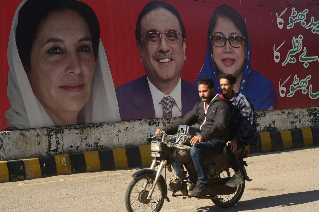 سائق دراجة نارية وركاب يمرون أمام ملصق الحملة الانتخابية لحزب الشعب الباكستاني في كراتشي قبل الانتخابات الوطنية في 8 فبراير/شباط. (ا ف ب)   