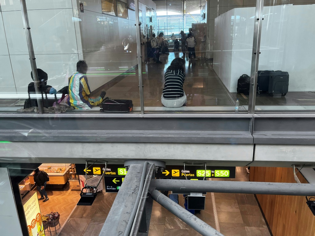 يجلس المهاجرون في منطقة العبور بمطار مدريد، الذي يكافح من أجل التعامل مع تدفق طالبي اللجوء (أ ف ب)   
