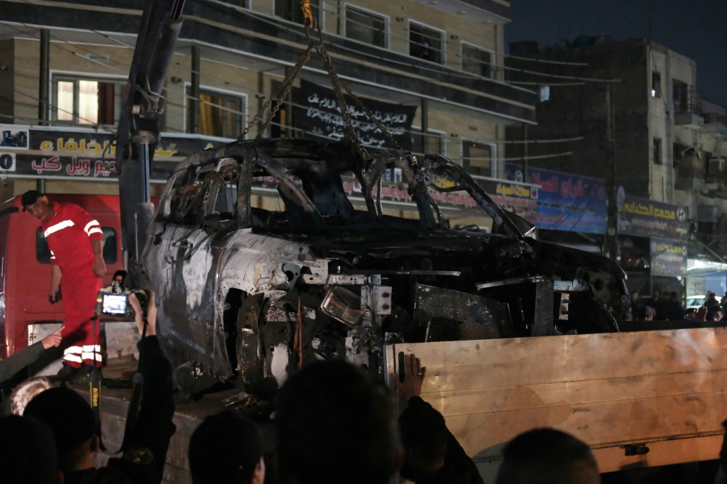 الناس يشاهدون إزالة السيارة التي أصيبت بغارة قاتلة بطائرة بدون طيار من أحد أحياء بغداد (ا ف ب)