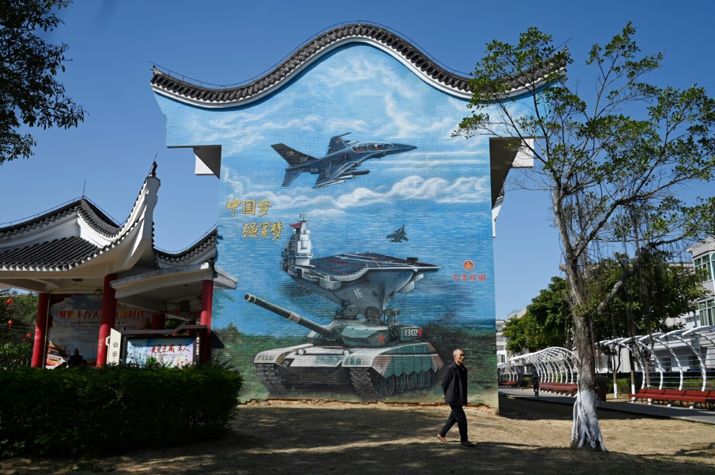 رجل يسير بجوار لوحة جدارية ذات طابع عسكري في حديقة عامة في جزيرة بينغتان، أقرب نقطة في الصين إلى جزيرة تايوان، في مقاطعة فوجيان جنوب شرق الصين في 14 كانون الثاني/يناير 2024 (أ ف ب)   