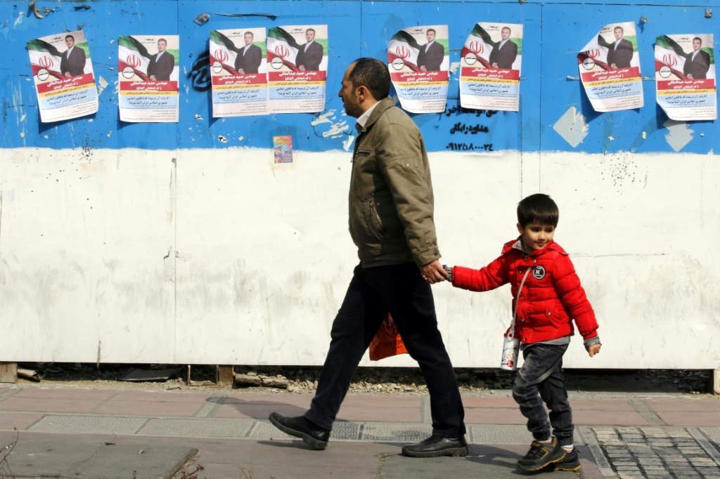 رجل وطفل يسيران أمام ملصقات الحملة الانتخابية التي تحمل صور مرشح برلماني خلال اليوم الأول من الحملة الانتخابية في طهران (أ ف ب)   