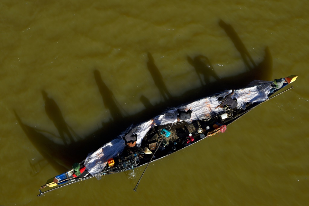 صورة التقطت في 4 كانون الثاني/يناير 2021 ويبدو فيها عدد من الرجال في قارب يسحبون شبكة لصيد الأسماك في نهر باساك، أحد فروع نهر ميكونغ، في بنوم بنه (أ ف ب)   